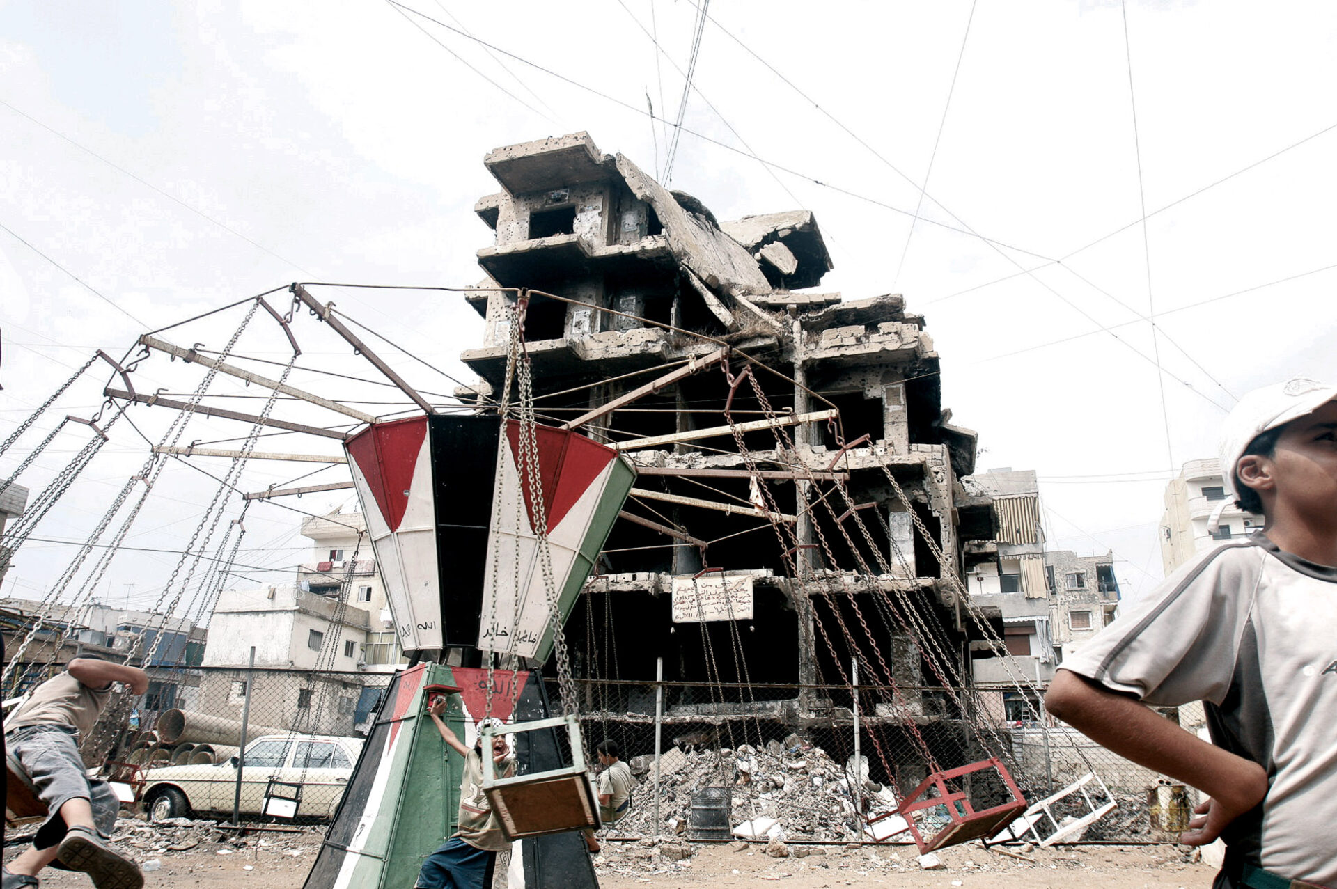 La fotografía muestra el campo de refugiados palestinos de Sabra y Chatila en Beirut, capital del Líbano. Decenas de niños juegan en un tiovivo decorado con la bandera palestina entre los escombros de edificios bombardeados. Este campo de refugiados es tristemente conocido por la matanza de 6.000 mujeres, niños y hombres perpetrada por las milicias falangistas libanesas con el apoyo del ejército Israelí, después de que milicianos islamistas asesinaran al presidente libanés y líder de la Falange libanesa Bechir Gemayel.