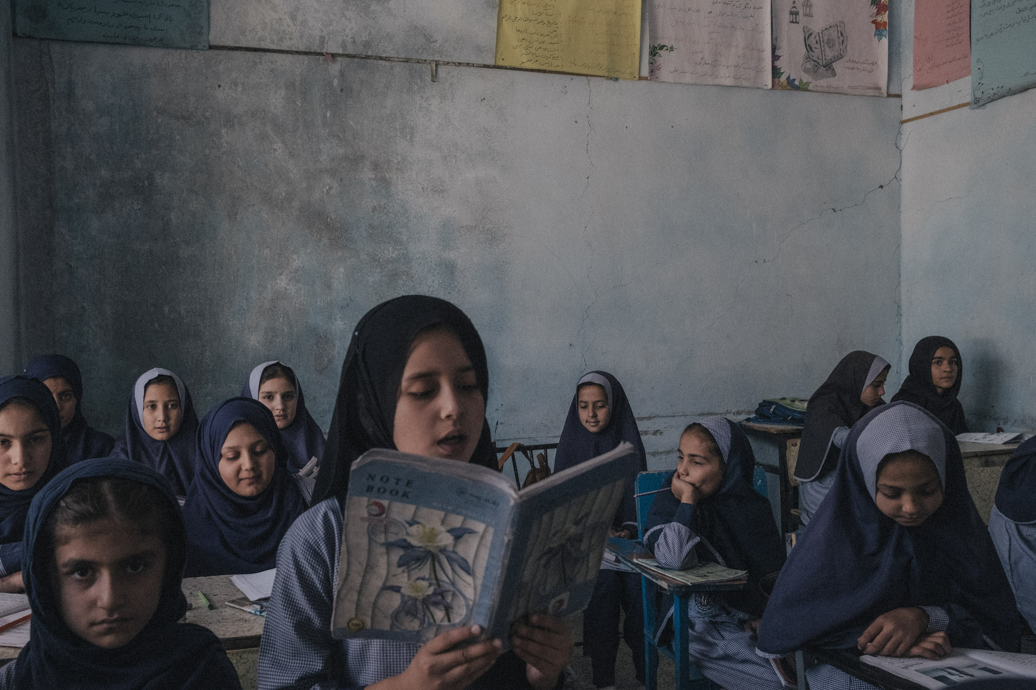 Un grupo de niñas está sentado en un aula de escuela primaria. Desde agosto de 2021, los talibanes han despojado sistemáticamente a mujeres y niñas del acceso a la educación en Afganistán, imponiendo restricciones cada vez más severas. La prohibición de que las niñas asistieran a la escuela secundaria se aplicó en marzo de 2022, seguida de la suspensión de las mujeres en las universidades en diciembre del mismo año. En enero de 2023, los talibanes intensificaron sus medidas represivas al impedir que las niñas realizaran los exámenes de ingreso a la universidad, revirtiendo por completo los avances logrados, incluso en provincias donde la participación femenina había superado a la masculina. Tras finalizar la educación primaria, la mayoría de las niñas no tiene otra opción que permanecer en casa y esperar un matrimonio concertado. Su posibilidad de trabajar fuera de los sectores de salud y educación es prácticamente nula. En conjunto, los decretos talibanes han confinado a mujeres y niñas a sus hogares, lo que equivale a una forma de encarcelamiento.