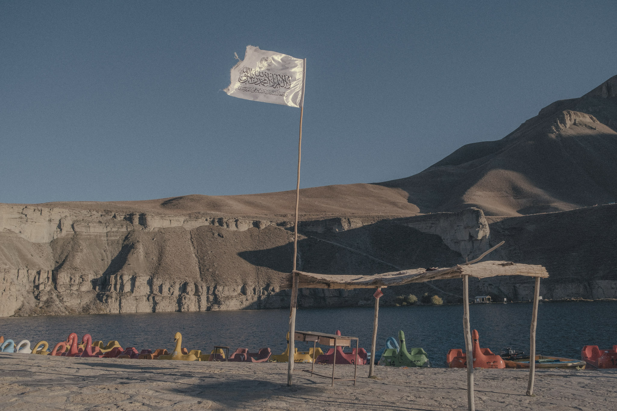 La bandera talibán ondea en el Parque Nacional Band-e-Amir, en la provincia de Bamyan, un destino al que cada año acuden miles de familias para disfrutar de sus lagos azul cristal y acantilados imponentes. En agosto de 2023, los talibanes prohibieron la entrada de mujeres al parque, como parte de su campaña continua para excluir a las mujeres de la vida pública. Desde 2021, los talibanes han prohibido la educación femenina y la mayoría de las formas de empleo, además de imponer estrictas restricciones a su movilidad y apariencia. La prohibición se produjo poco después de que Mohammad Khalid Hanafi, ministro talibán para la promoción de la virtud y la prevención del vicio, afirmara que las mujeres que visitaban Band-e-Amir no llevaban correctamente el hiyab obligatorio.