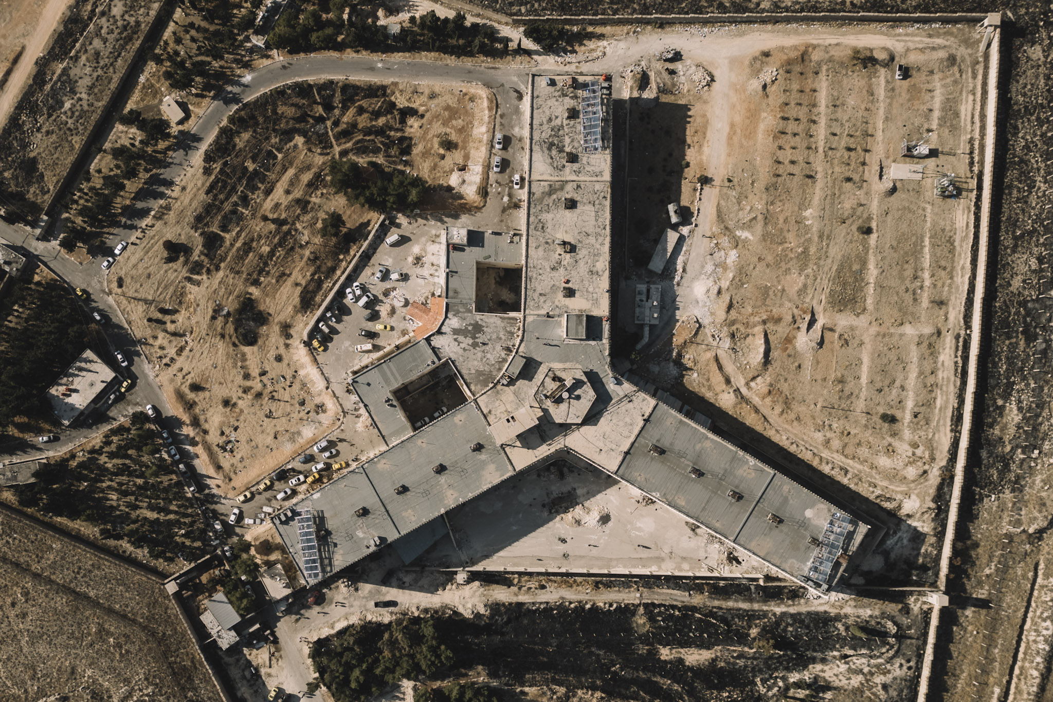 Una vista aérea de la prisión de Sednaya, situada a las afueras de Damasco, revela una instalación que en su día albergó a miles de personas detenidas. Inaugurada el 8 de diciembre, se hizo tristemente famosa como centro de detención y lugar de exterminio bajo el régimen de Assad. Durante el colapso del régimen, las fuerzas de Hayat Tahrir al-Sham (HTS) asaltaron las prisiones del régimen, incluida Sednaya, y liberaron a los detenidos. El complejo penitenciario, con capacidad para entre 10 000 y 20 000 presos, se erigía como un sombrío símbolo de la represión. Desde 2011 hasta su cierre, Sednaya fue el destino final de disidentes pacíficos y desertores militares acusados de oponerse al régimen. Miles de personas perdieron la vida en la red de prisiones de tortura de Siria, mientras que otras innumerables sufrieron abusos horribles, como palizas, violaciones y electrocución, a menudo para coaccionarles a confesar falsamente. Las condiciones eran inhumanas: los detenidos sufrían hambre, heridas sin tratar y muertes causadas incluso por infecciones leves. El hacinamiento, la falta de luz solar y la amenaza constante de violencia dejaron a muchos con graves secuelas psicológicas. El oscuro legado de Sednaya perdura como un crudo recordatorio de la brutalidad del régimen.