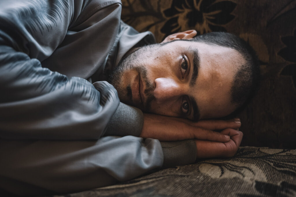 Después de siete años en prisión, Mohamed Khaled Krayem por fin es libre. Su familia está feliz, pero a él le cuesta pensar en el futuro, ya que debe acudir a citas médicas para recuperarse tras su liberación. “Nos golpeaban con tubos de hierro y plástico en las manos y los pies”, cuenta Mohamed. Ahlan wa sahlan, es una expresión árabe que significa bienvenido. Los entrevistados pronuncian estas palabras como si se refirieran a un viejo conocido: ahlan wa sahlan. Y otra más: dulab, que significa rueda. Este método de tortura, aunque sencillo, se convirtió en uno de los sellos distintivos del régimen: sentar al prisionero dentro de una rueda, inmovilizarlo y golpearlo. “Te ponían boca arriba dentro del neumático y empezaban a golpearte los pies con tiras hechas con otro neumático que habían cortado”, explica Mohamed, el superviviente con los dientes rotos. En la foto, Mohamed adopta la misma postura en la que solía dormir mientras estaba en prisión. Después de siete años tumbado en la misma postura, su memoria muscular, aún fresca desde su liberación hace solo unos días, reproduce instintivamente las posiciones que se veía obligado a adoptar en su celda. La falta de espacio y la naturaleza repetitiva de esos movimientos hacen que recuerde exactamente cómo se tumbaba y dormía en la cárcel de Sednaya.